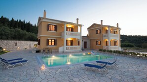A two-story house with a swimming pool, stone patio, and lounge chairs. - FLORENA VILLAS (Lefkada)