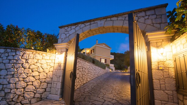 A stone archway leading to a house with a stone wall on one side and a light fixture on the other. - FLORENA VILLAS (Lefkada)
