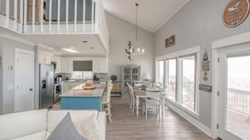Een ruime woonkamer met een hoge plafond, een eettafel met stoelen, een keuken met moderne apparatuur en een balkon met uitzicht.