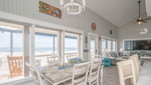 A spacious dining area with a view of the ocean, a cozy seating area with a television, and a ceiling fan.