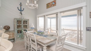 A dining area with a view of the beach, white furniture, and nautical decor.