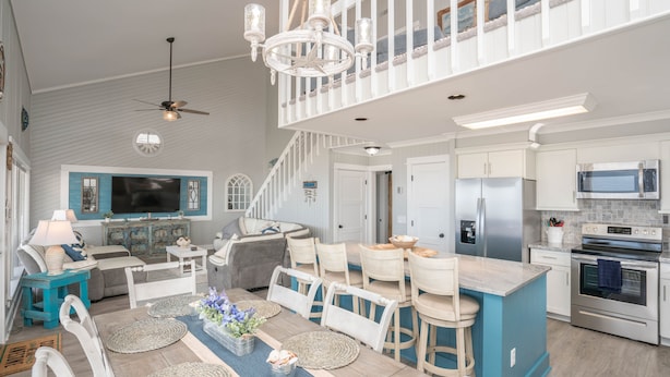 A spacious kitchen with a dining area, a staircase, and a living room with a TV.
