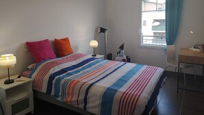 Een hotelkamer met een bed, nachtlampjes, een bureau en een raam met gordijnen.