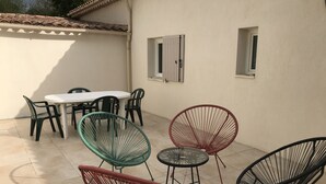 A patio area with a round table and multiple chairs, a tiled floor, and a white wall with windows. - Luberon: between Aix and Lourmarin (VILLELAURE)