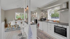 Eine moderne Küche mit weißen Schränken, einer schwarzen Arbeitsplatte und einer Edelstahl-Dunstabzugshaube. Es gibt einen Essbereich mit weißen Stühlen und einem Tisch, und ein großes Fenster sorgt für natürliches Licht.