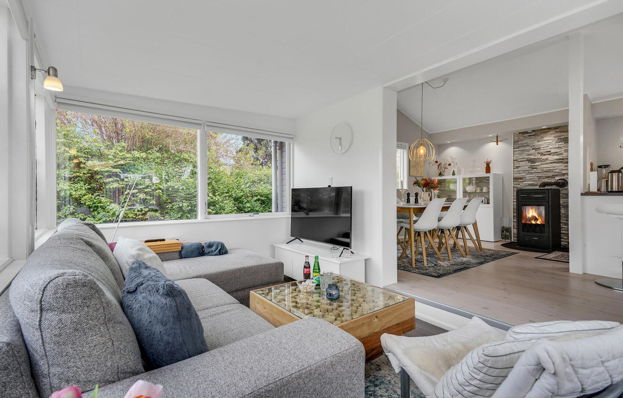 A modern living room with a sofa, coffee table, and TV. There is a kitchen area with a fireplace and dining space.