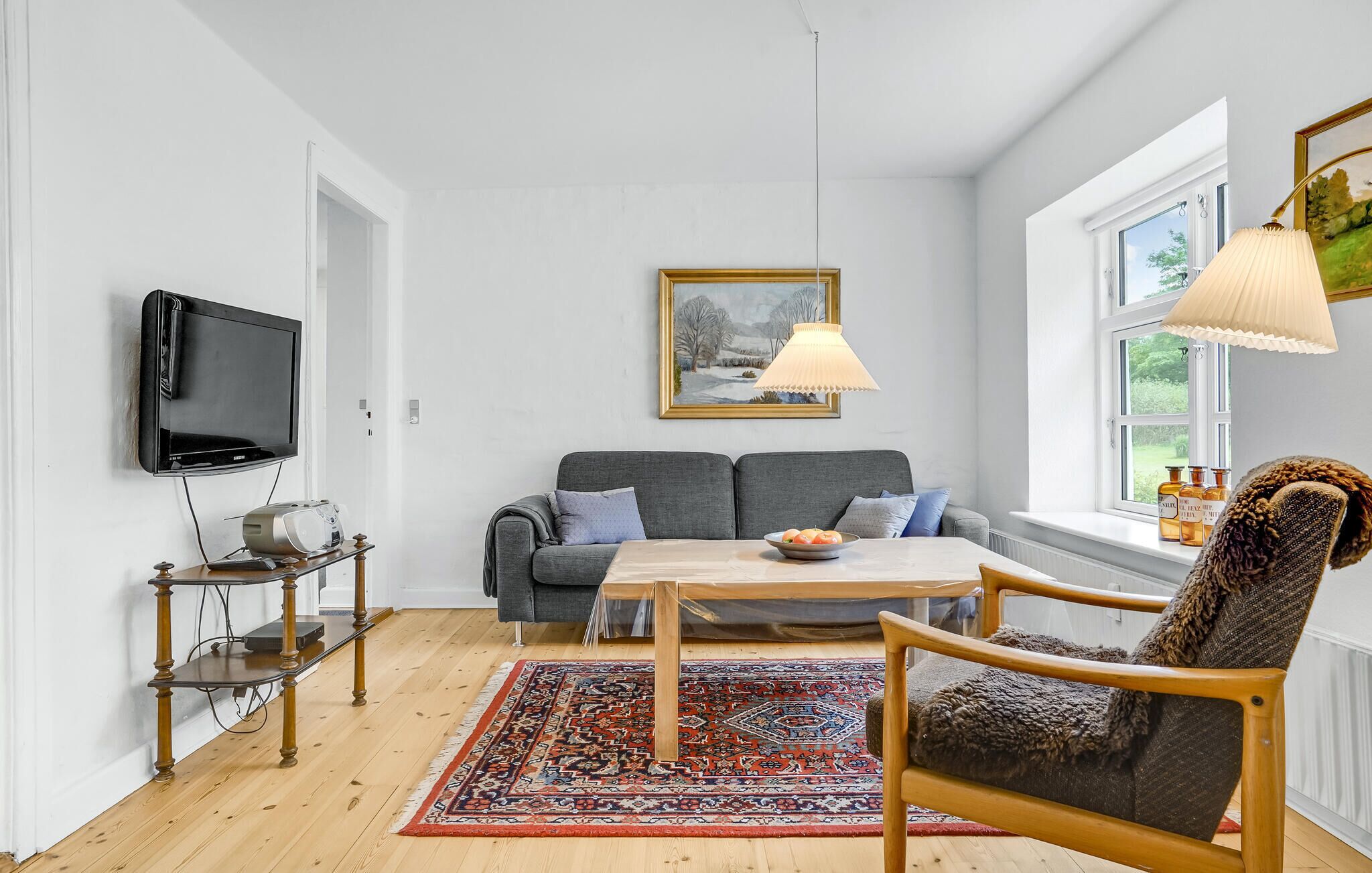 A living room with a grey sofa, a wooden coffee table, a patterned rug, a television, and a painting on the wall.