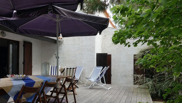 Een terras met een tafel en stoelen, overdekt door een grote parasol, omringd door groen.