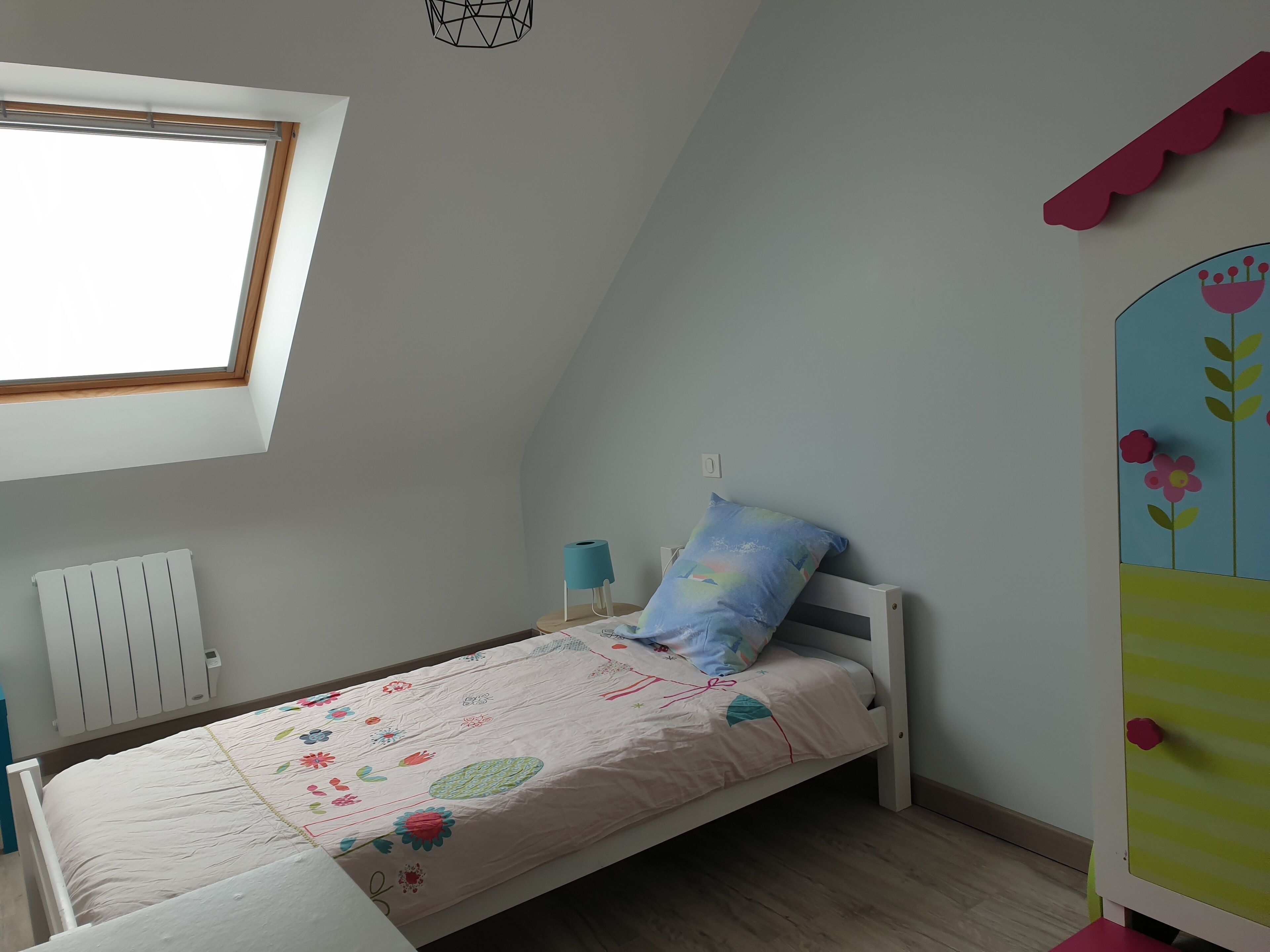Et børneværelse med en enkeltseng, et vindue, en radiator og en væg med dekorativ panel.