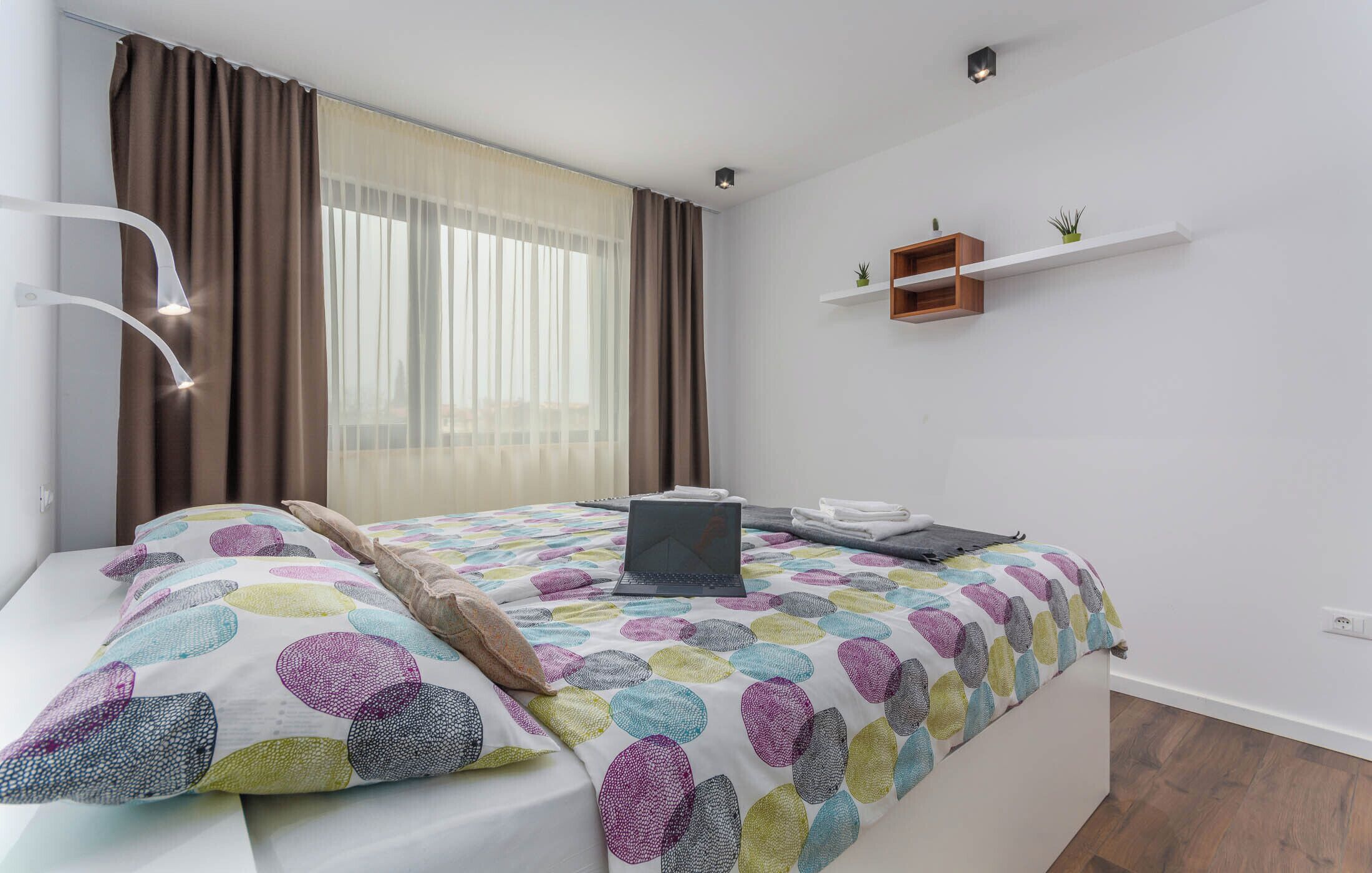 Une chambre à coucher avec un lit, un ordinateur portable et une petite étagère avec des plantes.