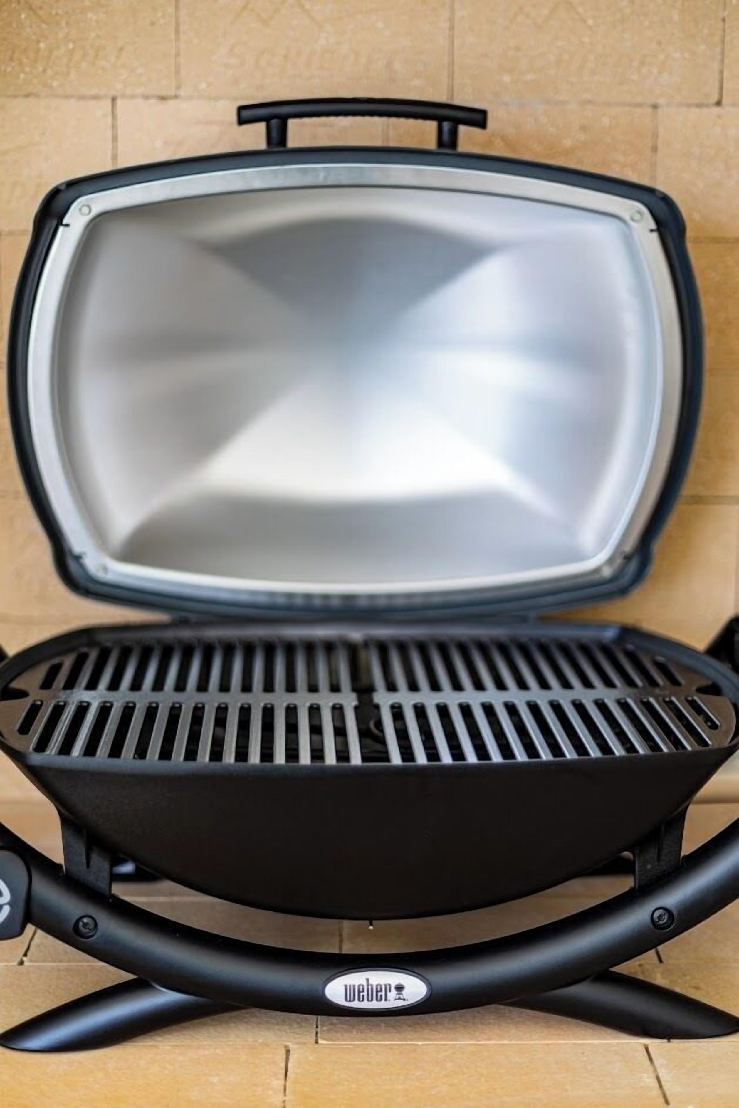 A portable grill with a black handle and a metal grate, placed on a tiled floor.