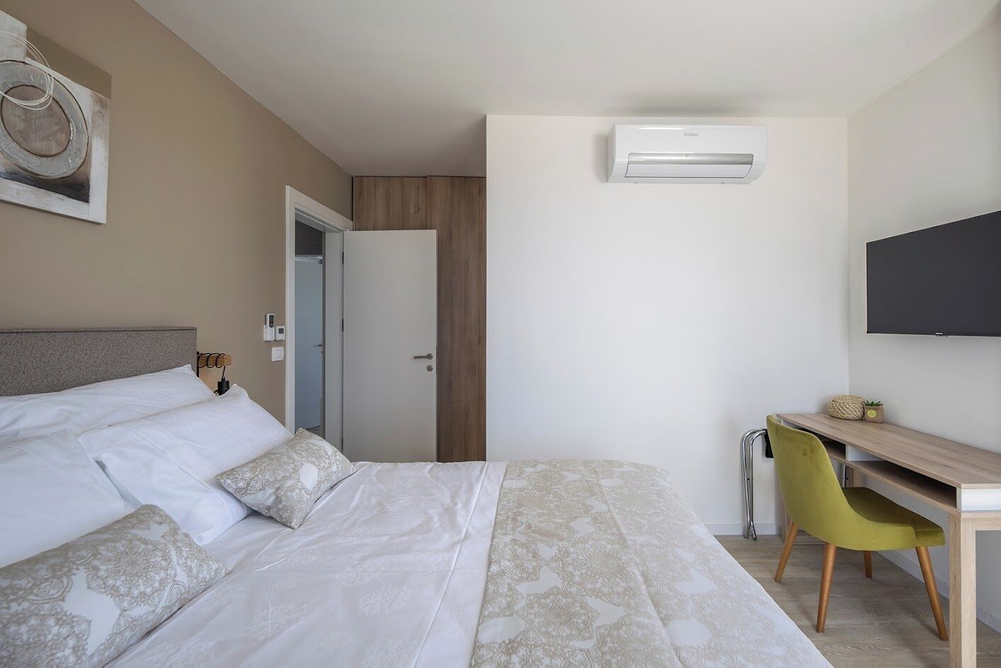 Een hotelkamer met een bed, een bureau, een stoel, een airconditioner en een televisie.