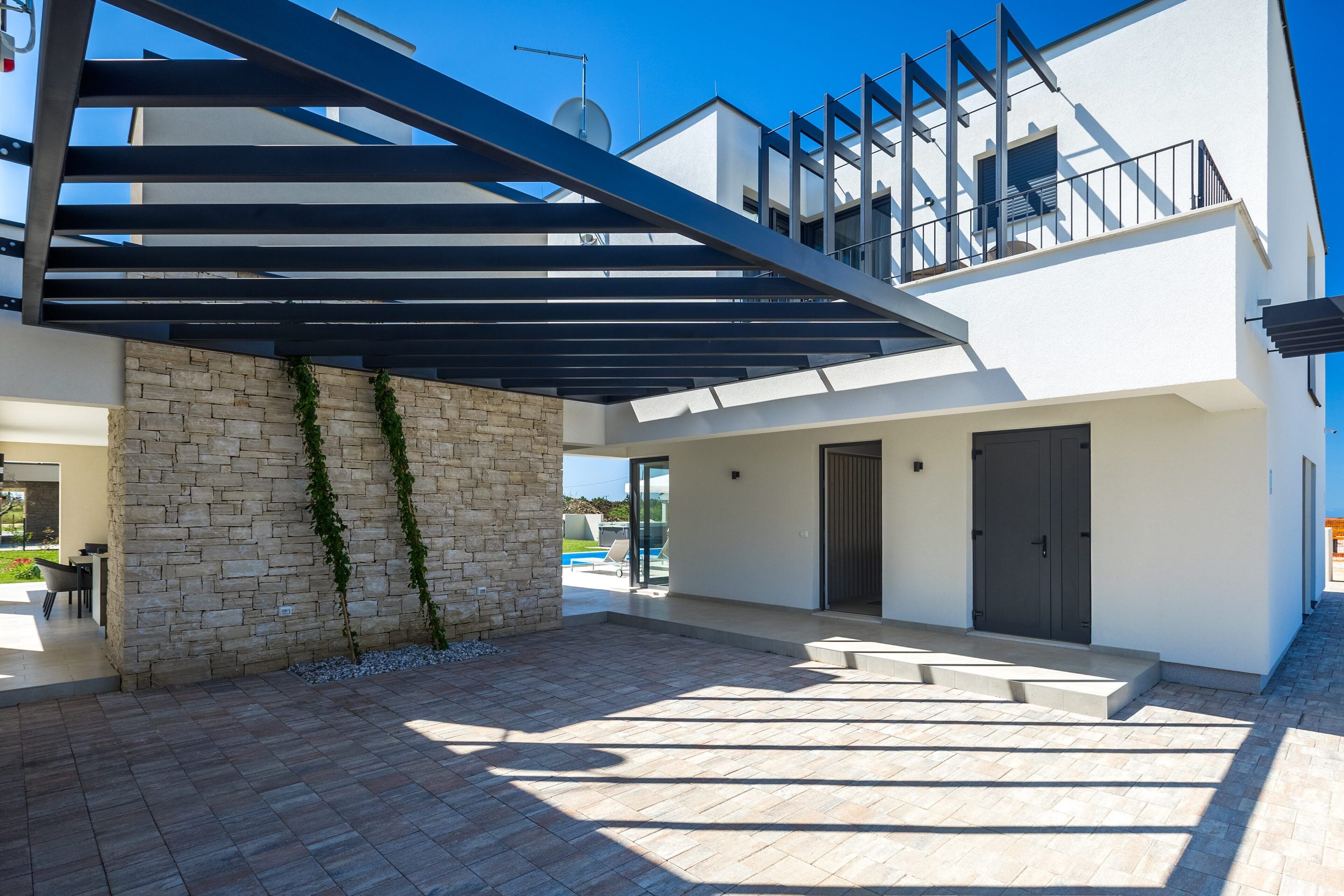 A modern house with a covered patio, stone walls, and a staircase leading to an upper level.