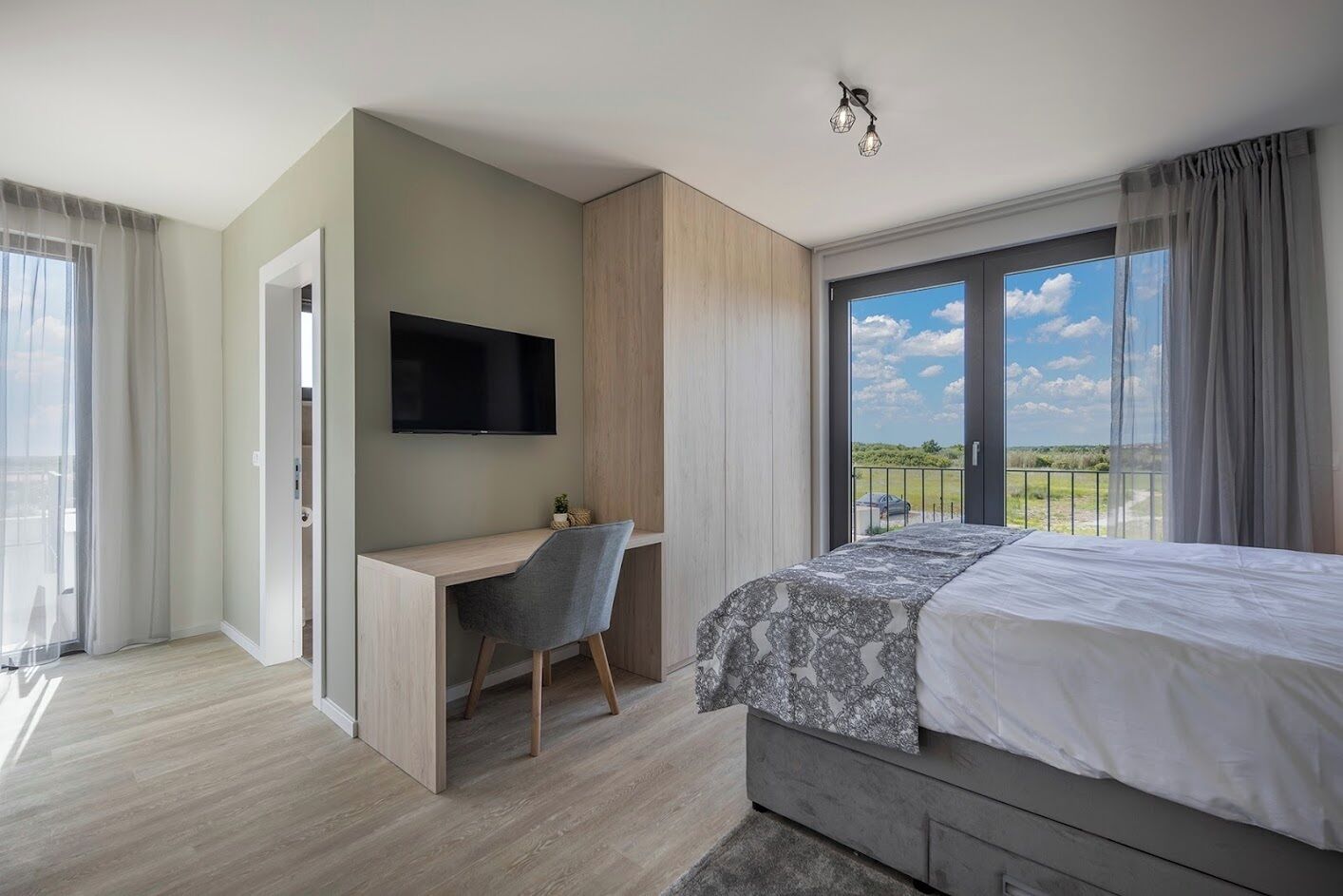 A modern bedroom with a bed, a desk, and a TV.