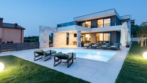 Una casa moderna de dos pisos con piscina, mobiliario exterior y césped cuidado.