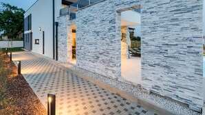 Un edificio moderno con fachada de piedra, balcón de cristal y un camino pavimentado.