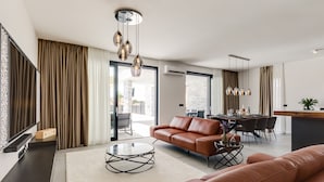 Una sala de estar moderna con un sofá de cuero marrón, una mesa de centro de vidrio y un comedor con una mesa y sillas de madera.