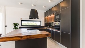Una cocina moderna con una isla central, muebles oscuros y un ventanal grande.