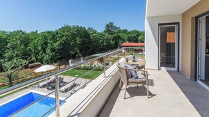 Un balcón con piscina, mobiliario exterior y vista a un edificio de techos rojos y árboles.