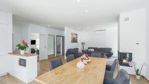 Un espacio habitable moderno con una mesa de comedor de madera en el centro, sofás grises y una pequeña zona de cocina con microondas.