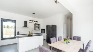 Une cuisine moderne dotée d’un îlot central, d’appareils électroménagers noirs et d’un coin repas avec des chaises violettes.
