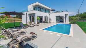 Une maison moderne dotée d’une piscine, d’un espace salon extérieur et d’une pelouse bien entretenue.