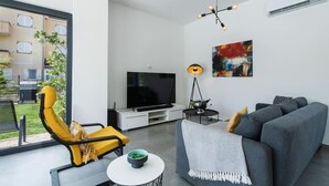 Un salon moderne avec un canapé gris, un fauteuil jaune et un téléviseur à écran plat.