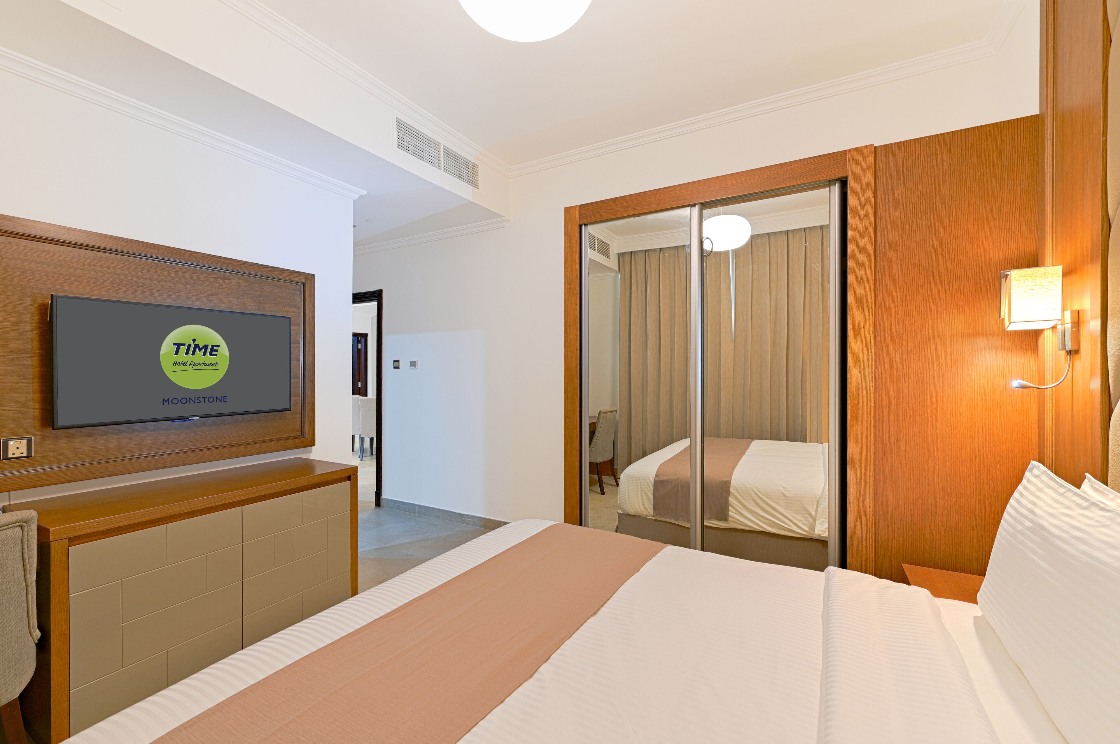 Ein Hotelzimmer mit einem Bett, einem an einer Holzkonsole montierten Fernseher, einem Spiegel und einem Schiebetürenschrank.