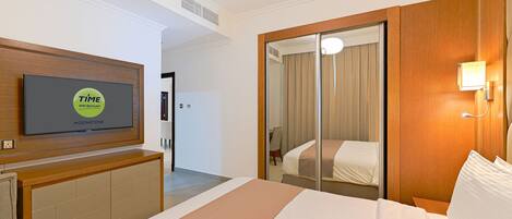 A hotel room with a bed, a TV mounted on a wooden console, a mirror, and a sliding door closet.