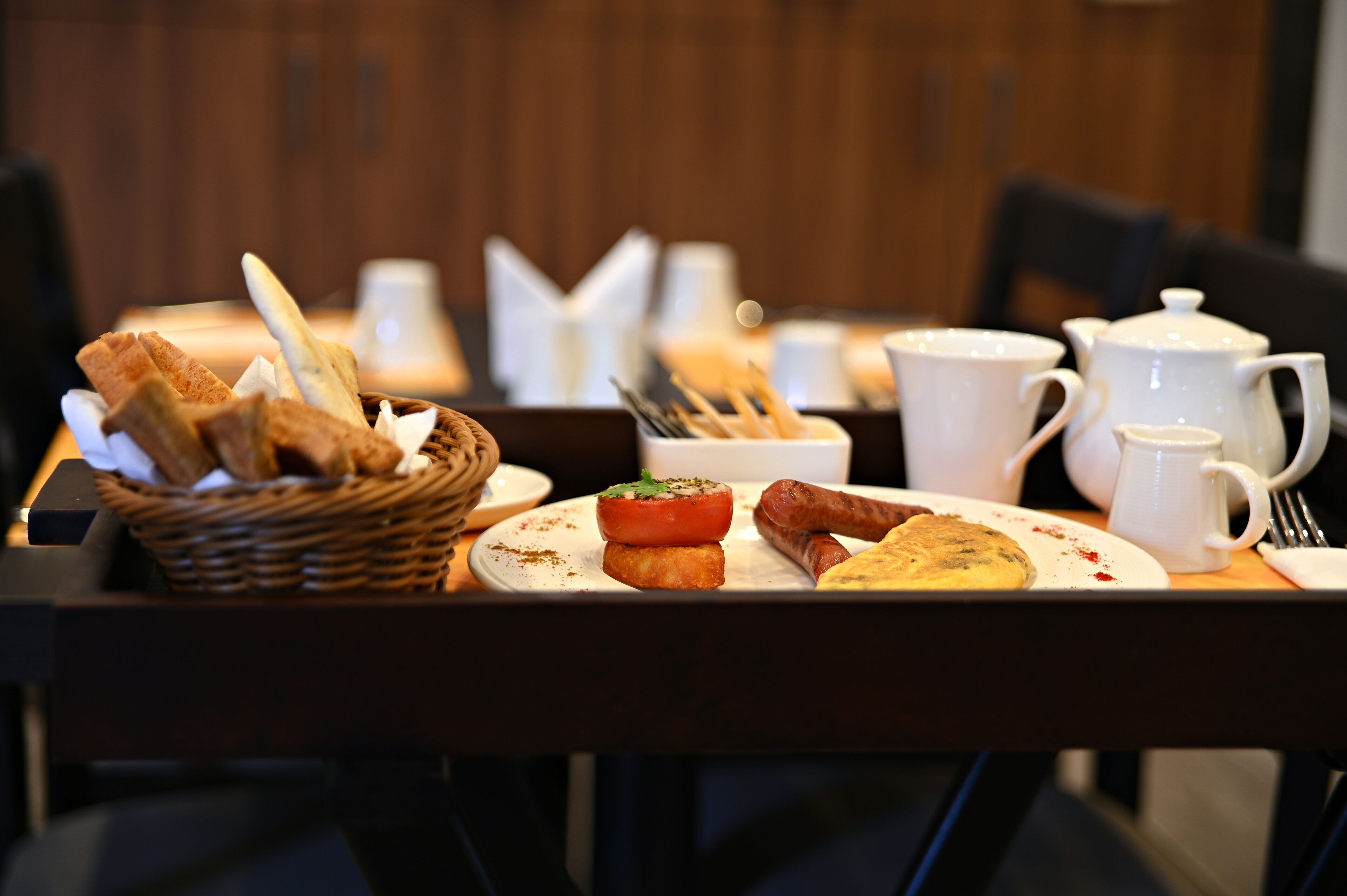 Une table de petit-déjeuner avec du pain, des saucisses, des tomates et une assiette de nourriture.
