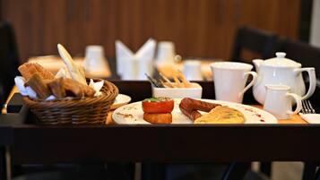 Une table de petit-déjeuner avec du pain, des saucisses, des tomates et une assiette de nourriture.