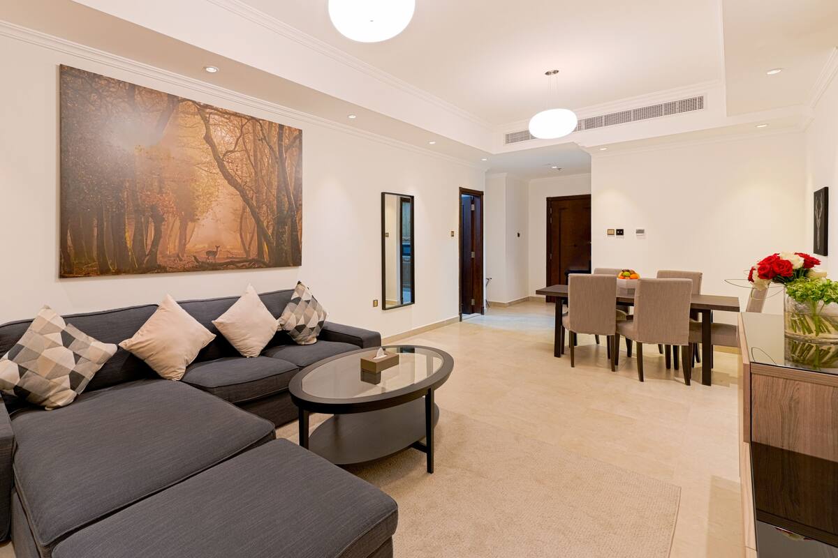 Ein modernes Wohnzimmer mit grauem Sofa, einem Glastisch und einem Essbereich mit Holztisch und Stühlen.