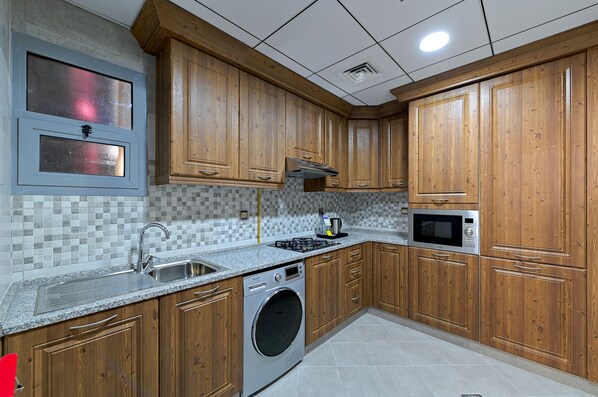 Une cuisine avec des meubles de rangement en bois, un lave-linge encastré, un four à micro-ondes et un revêtement mural en carreaux.