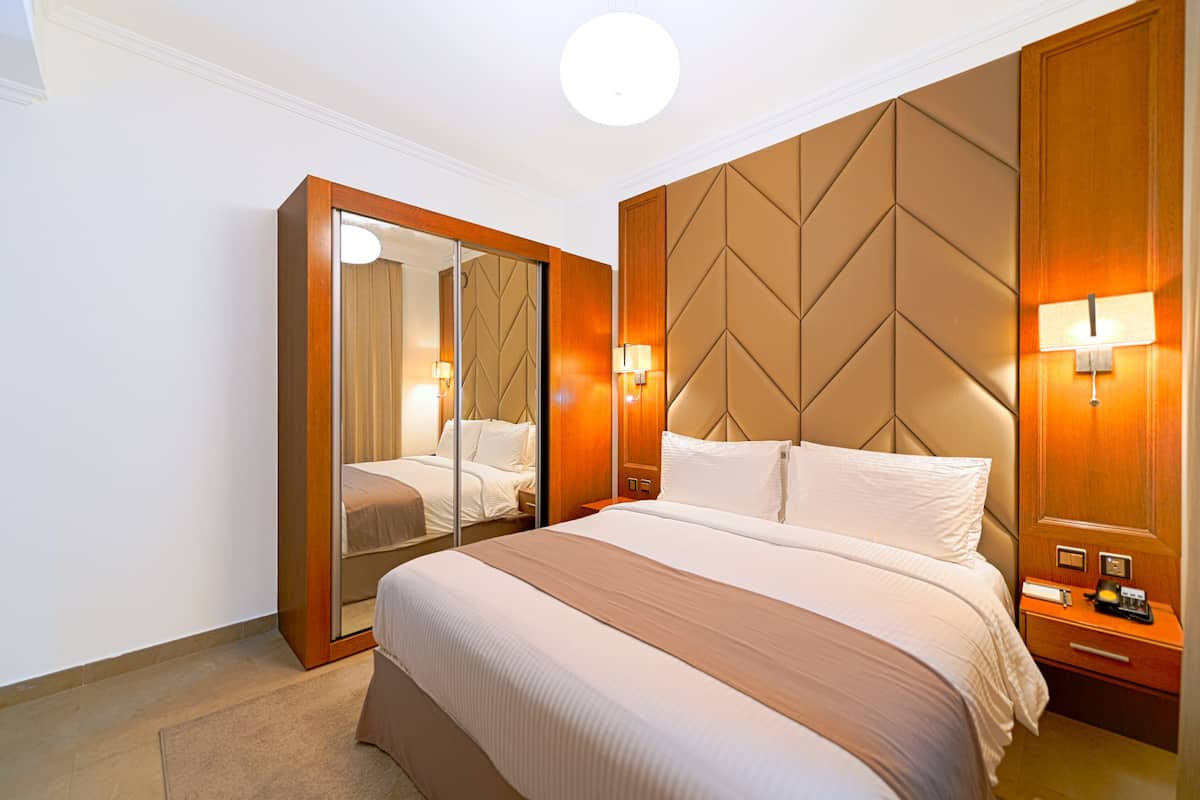 Ein Hotelzimmer mit einem großen Bett, einem hölzernen Kopfteil, einem Spiegel und Nachttischlampen.