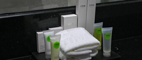 A hotel bathroom with a black countertop displaying toiletries, including a white towel, a green bottle, and a white box labeled "TIME HOTELS".