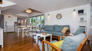 A spacious living area with a grey sofa, wooden chairs, a small table, and a kitchen in the background. - Villa Ferenc Zadarvillas (Rovinj)