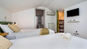A hotel room with two beds, a TV mounted on the wall, a shelf with decorative items, and an air conditioning unit. - Villa Ferenc Zadarvillas (Rovinj)