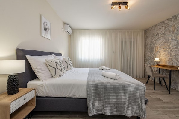 A bedroom with a bed, bedside table, lamp, and a stone wall.