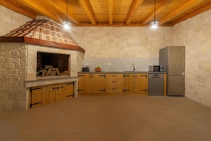 A rustic kitchen with a stone fireplace, wooden cabinets, and a stainless steel refrigerator.