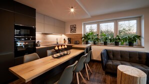 A modern kitchen with a wooden dining table, chairs, a built-in oven, and a window with potted plants. - Radvanice Kcg351 in Radvanice (Radvanice)