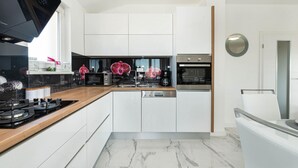 A modern kitchen with white cabinetry, a wooden countertop, a built-in microwave, a coffee maker, and a stainless steel oven. - Villa Silentium Zadarvillas (Benkovac)
