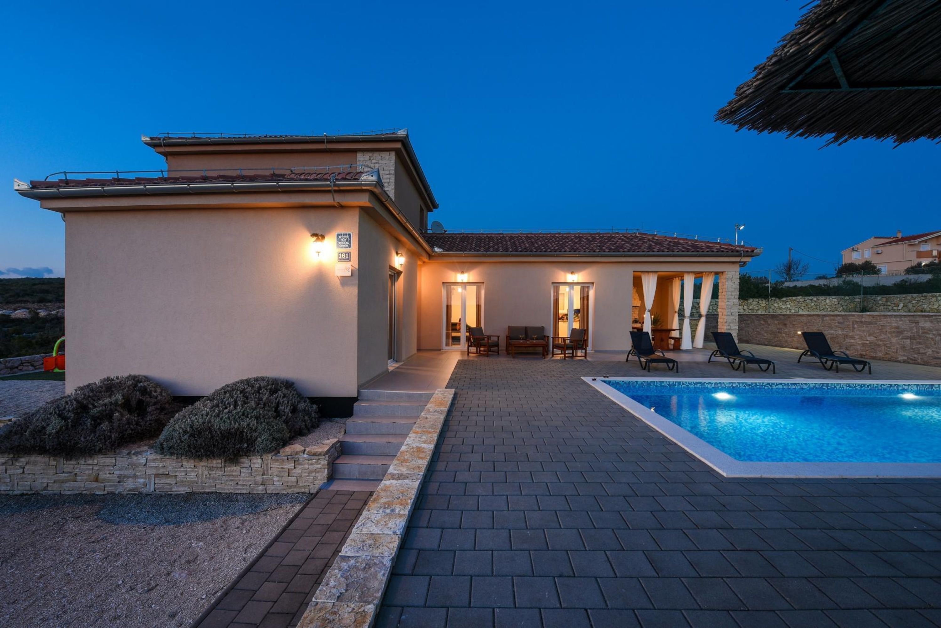 Ein modernes Haus mit Swimmingpool, Sitzgelegenheiten im Freien und einer Steinmauer.