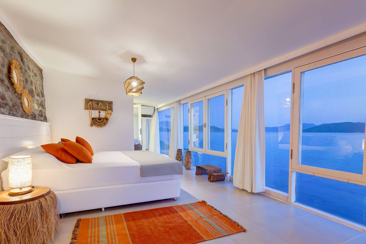 Un dormitorio espacioso con una cama grande, vista al mar y una lámpara de araña moderna.