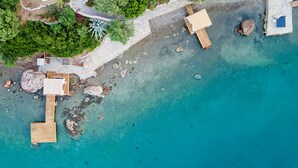 An aerial view of a beachfront property with wooden deck structures, clear turquoise water, and surrounding greenery. - Casa Daracia (+15) (Marmaris)