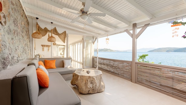 A modern, open-plan living area with a grey sofa, orange cushions, a round wooden coffee table, and a ceiling fan.