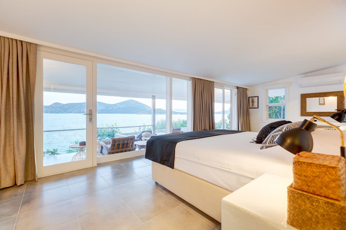 Un dormitorio con una cama grande, vista al mar y un balcón con mobiliario exterior.