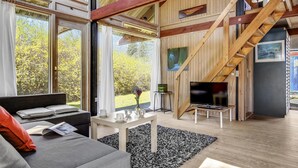 A modern living room with large windows, a staircase, and a flat-screen TV. - 2 bedroom cozy home in Dronningmølle (Dronningmølle)
