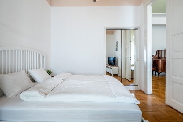 A bedroom with a large bed, a bedside table, a mirror, and a wooden floor.