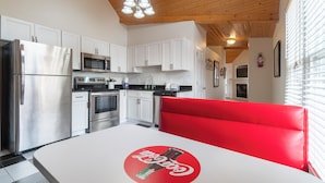 Een moderne keuken met witte kasten, roestvrijstalen apparatuur, een rode zithoek en een Coca-Cola logo op de tafel.