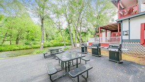 Ein Außenbereich mit Picknicktischen und Grills, umgeben von Bäumen und einem Gebäude mit einem Balkon.